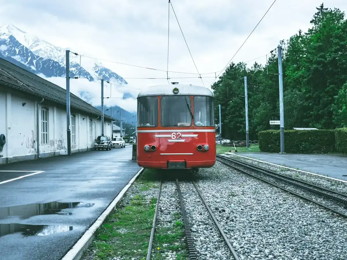 Un tren rojo alpino esperando en una estación de montaña con picos nevados detrás