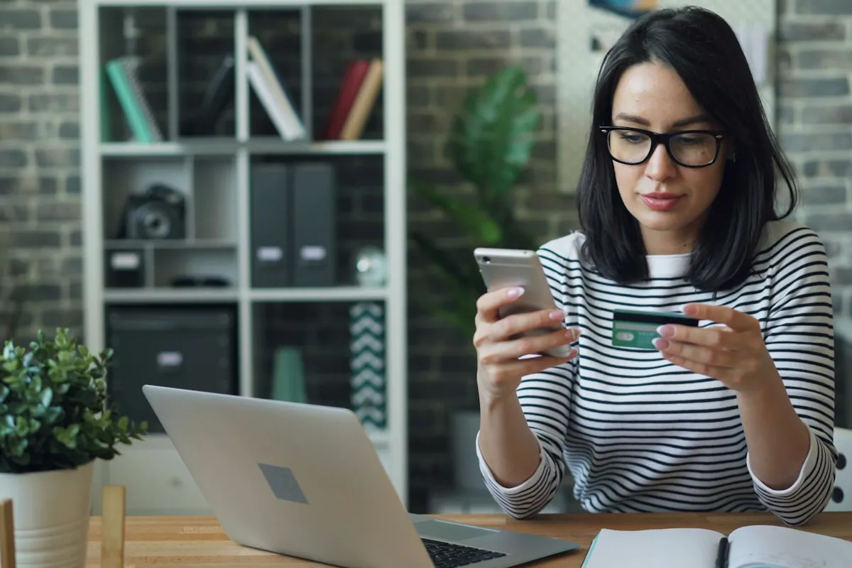 Woman holding a bank card and phone at her laptop