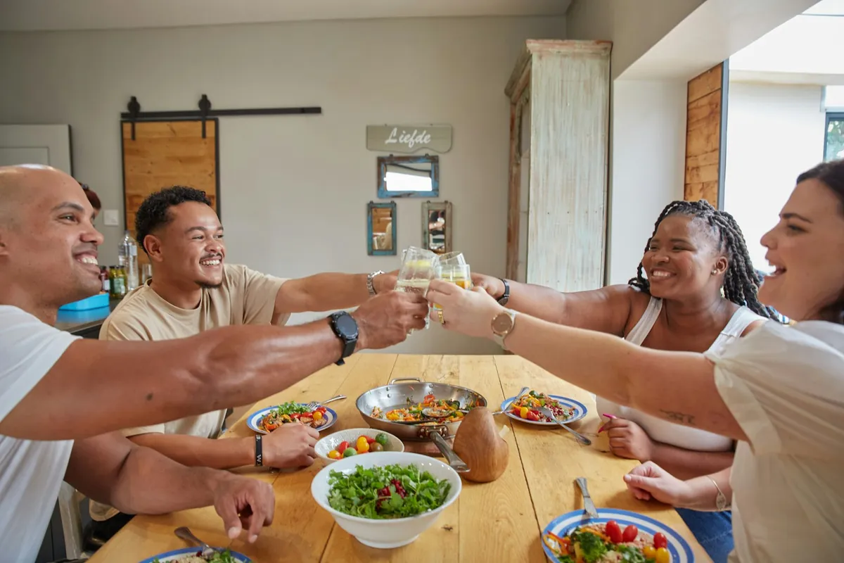 Housemates sharing a meal and a toast at a long table