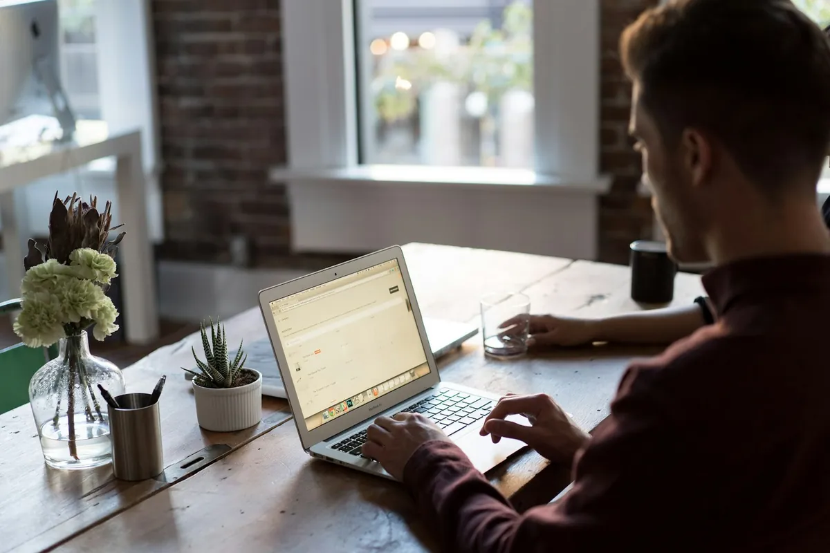Remote worker applying for jobs on a laptop at a wooden table
