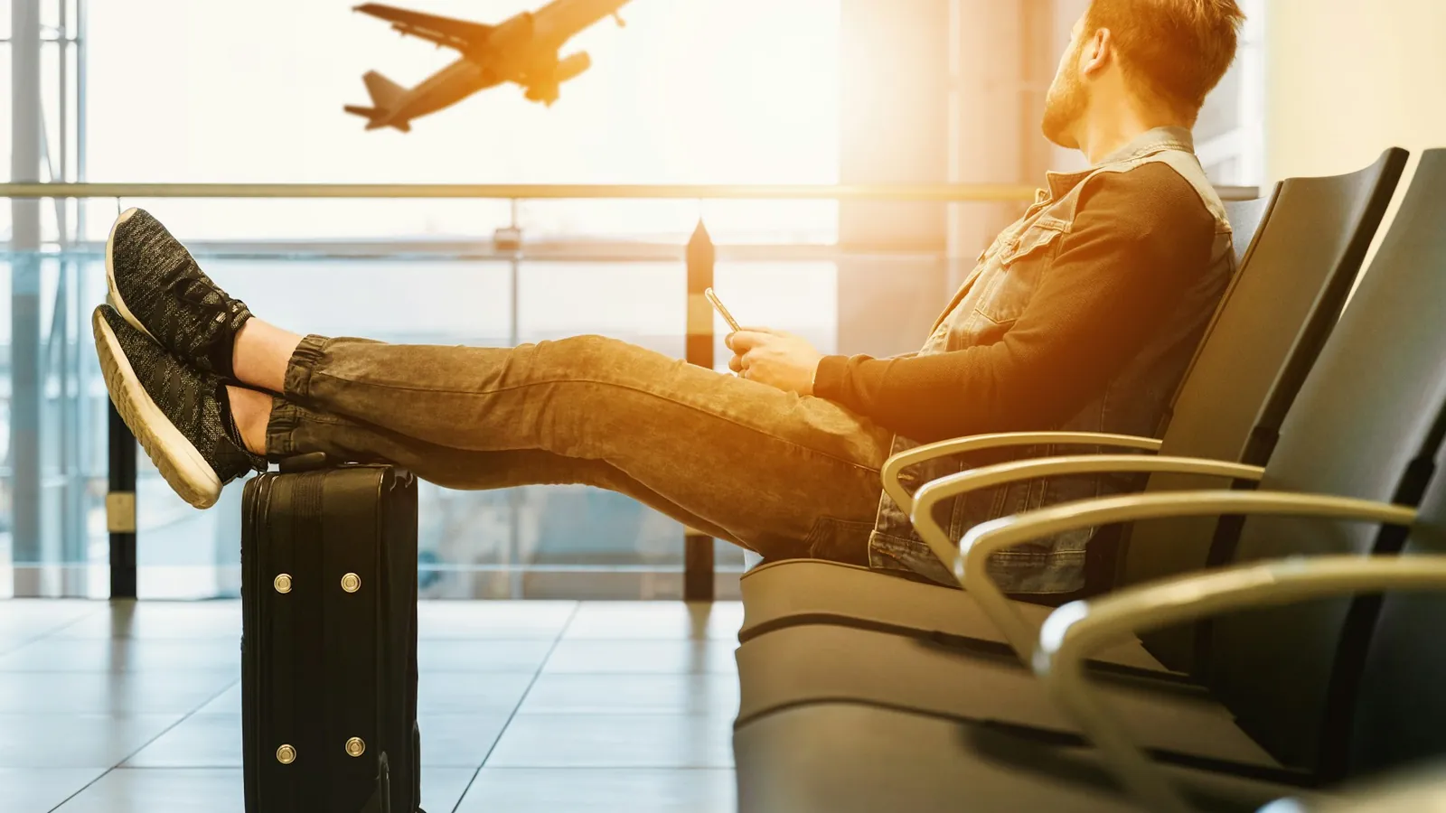 Traveler resting with feet on his suitcase while watching a plane take off at the airport