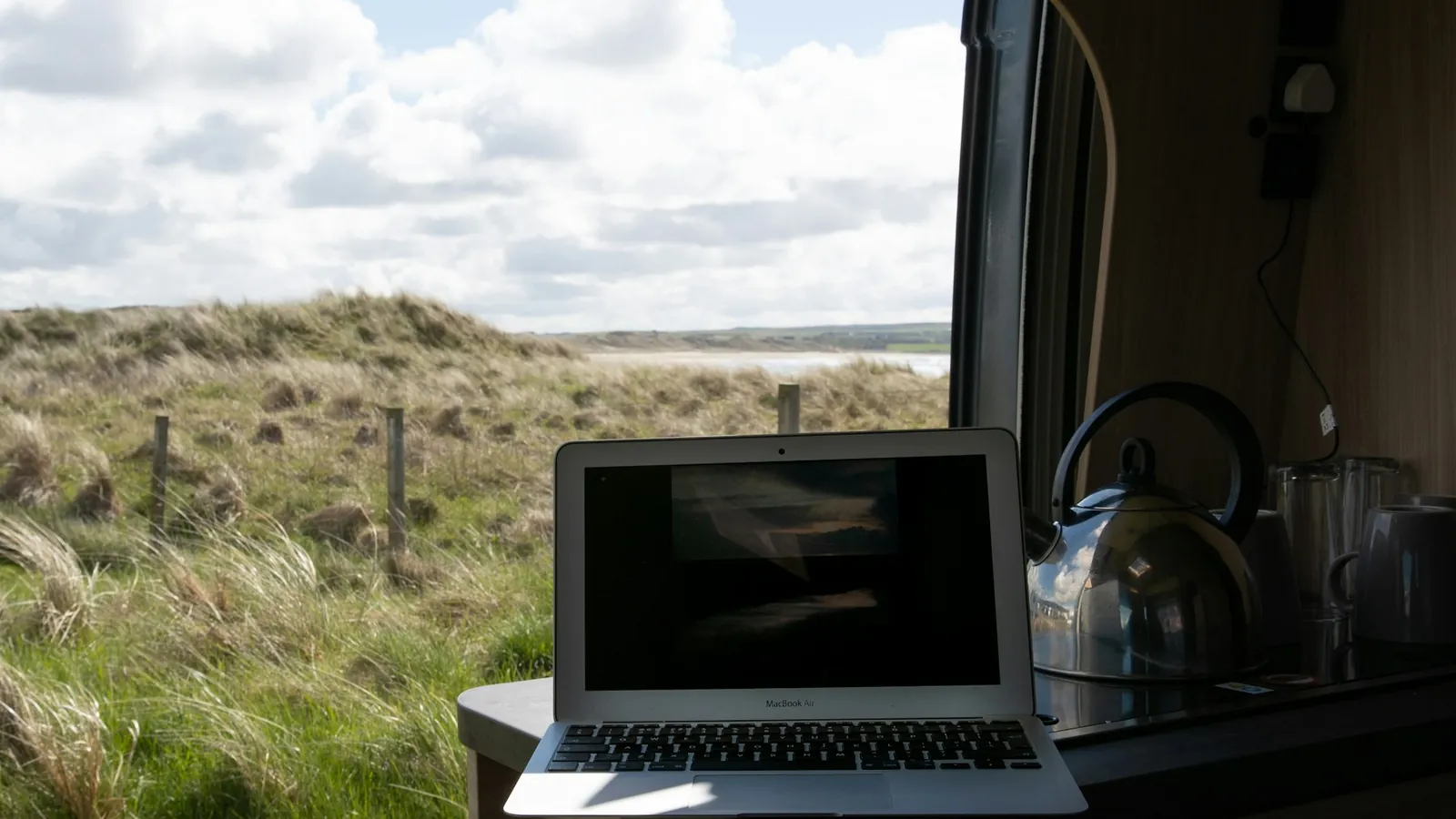 Laptop on a table inside a camper van with a view of the dunes outside