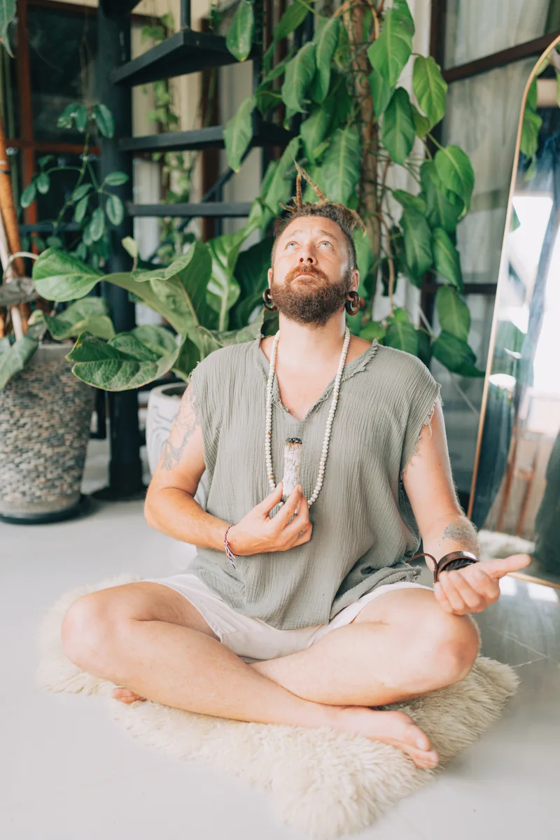 Chenzo, founder of NomadsToolsLab, meditating cross-legged among green plants