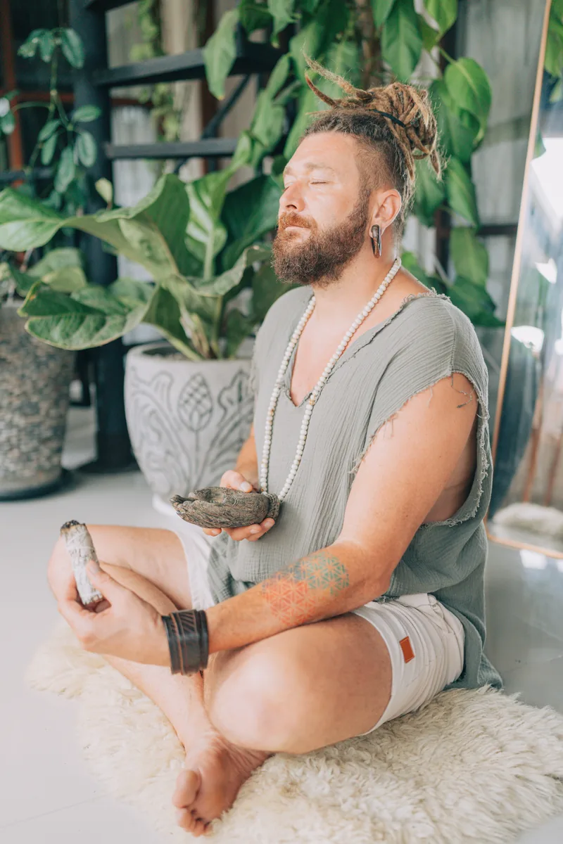 Chenzo, fundador de NomadsToolsLab, sentado meditando con los ojos cerrados junto a plantas verdes
