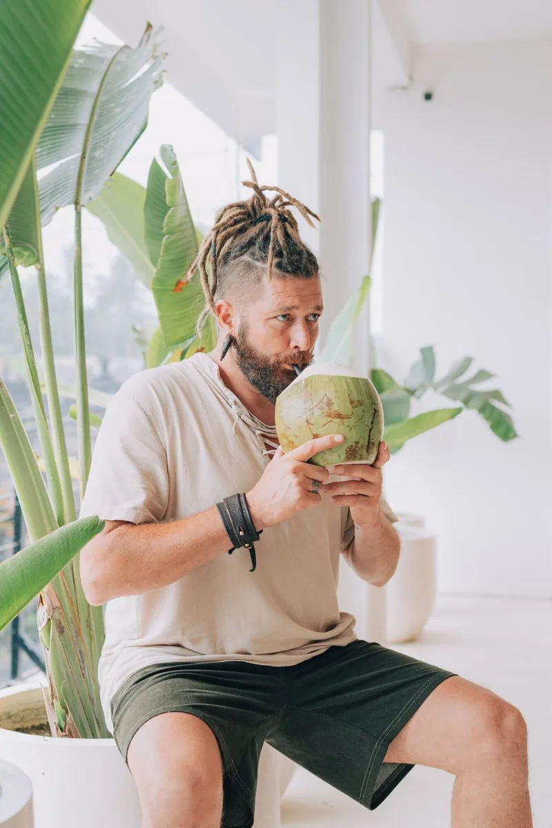 Chenzo, founder of NomadsToolsLab, drinking from a fresh coconut between tropical plants