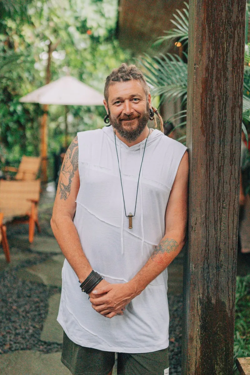 Chenzo, founder of NomadsToolsLab, leaning against a wooden post in a green garden