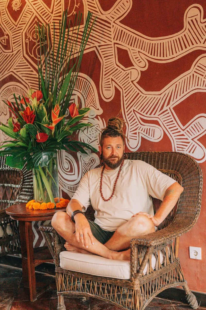 Chenzo, founder of NomadsToolsLab, sitting in a rattan chair next to tropical flowers
