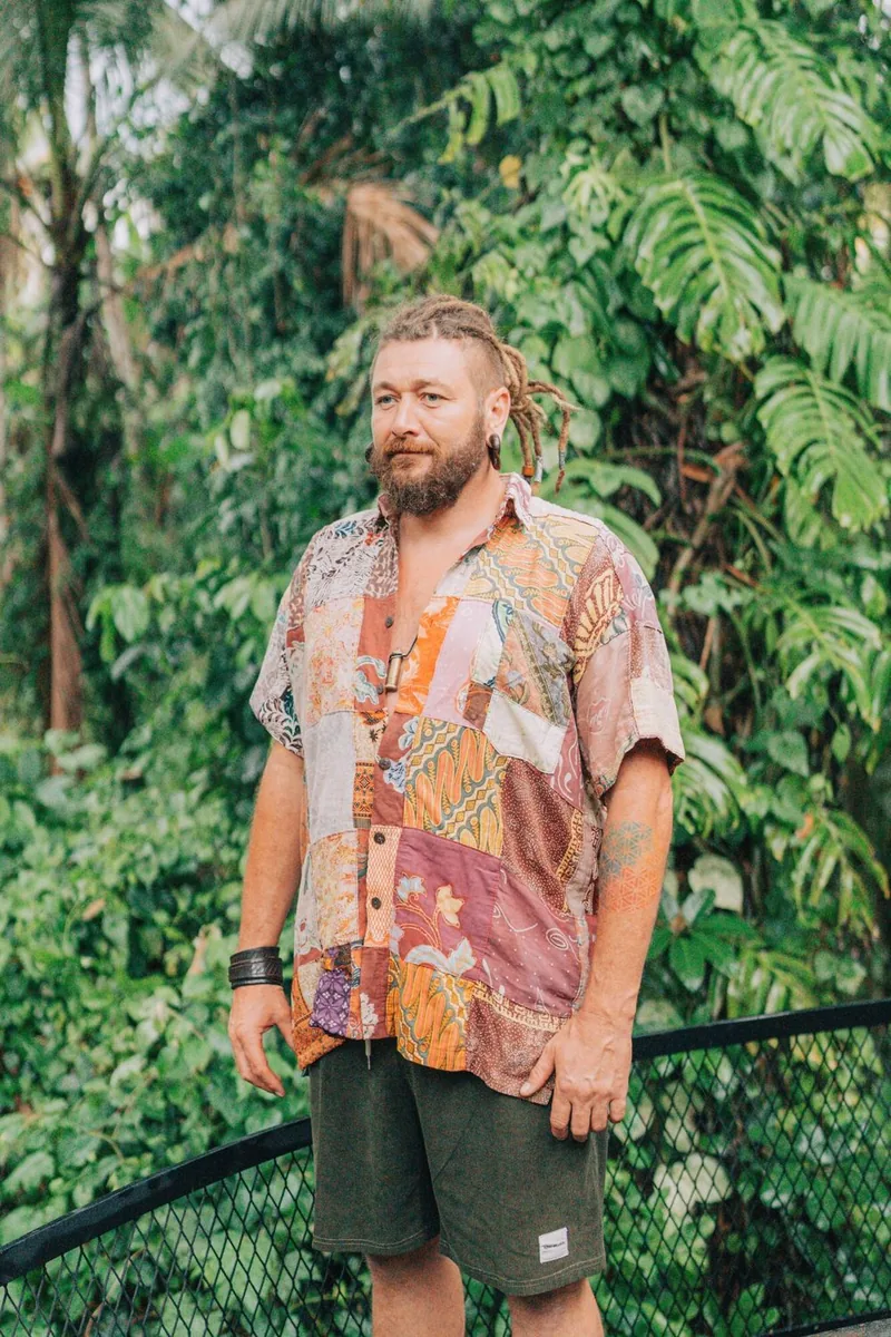 Chenzo, fundador de NomadsToolsLab, con una camisa de parches de colores entre árboles tropicales