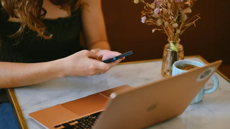Remote worker using a smartphone next to a laptop at a cafe table
