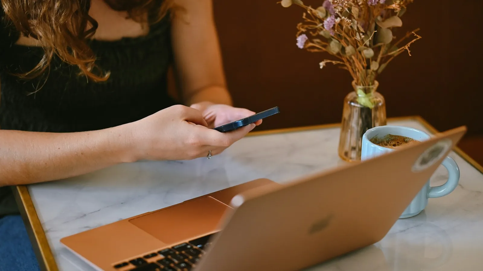 Remote worker using a smartphone next to a laptop at a cafe table