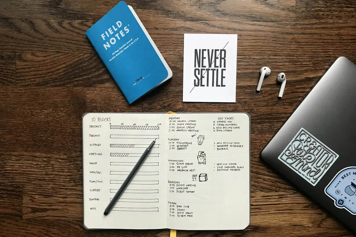 Notebook with a monthly plan next to a laptop and earbuds