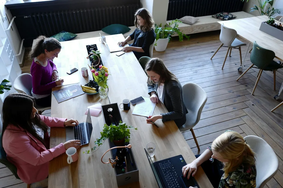 Menschen arbeiten an Laptops an langen Tischen in einem Coworking Space