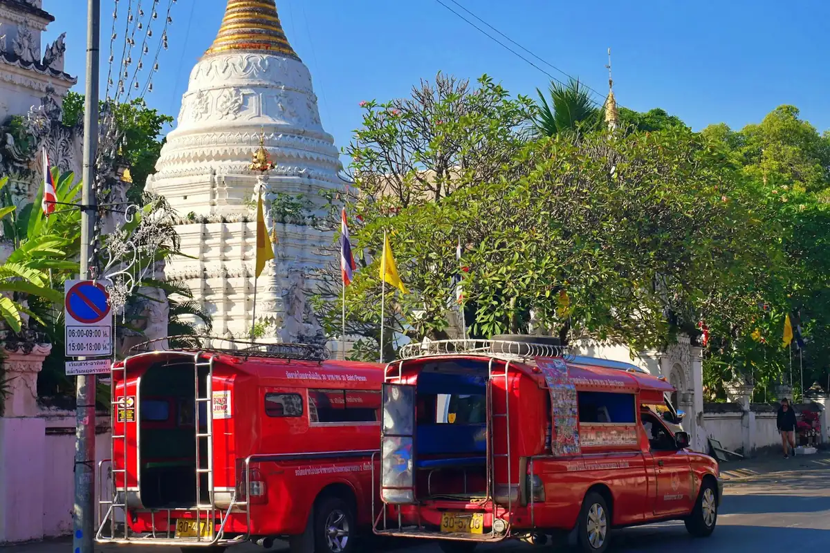 Red songthaew shared taxis parked in front of a white temple in Thailand