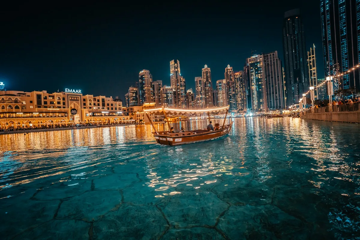 Un barco abra tradicional en el lago Burj frente al horizonte del centro de Dubái de noche