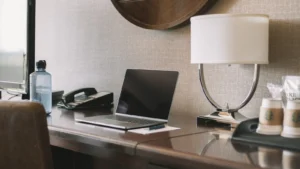 Laptop on a hotel room desk next to a lamp and coffee