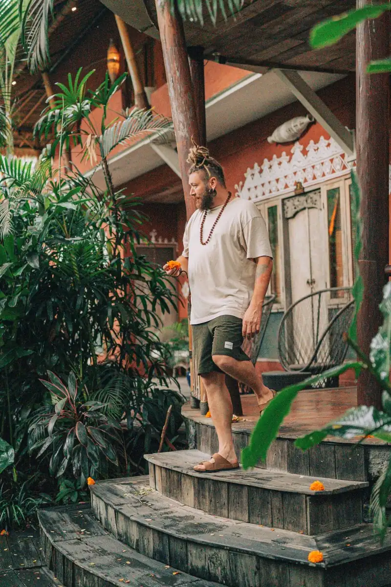 Chenzo walking down wooden steps at a traditional Balinese building holding orange flower petals