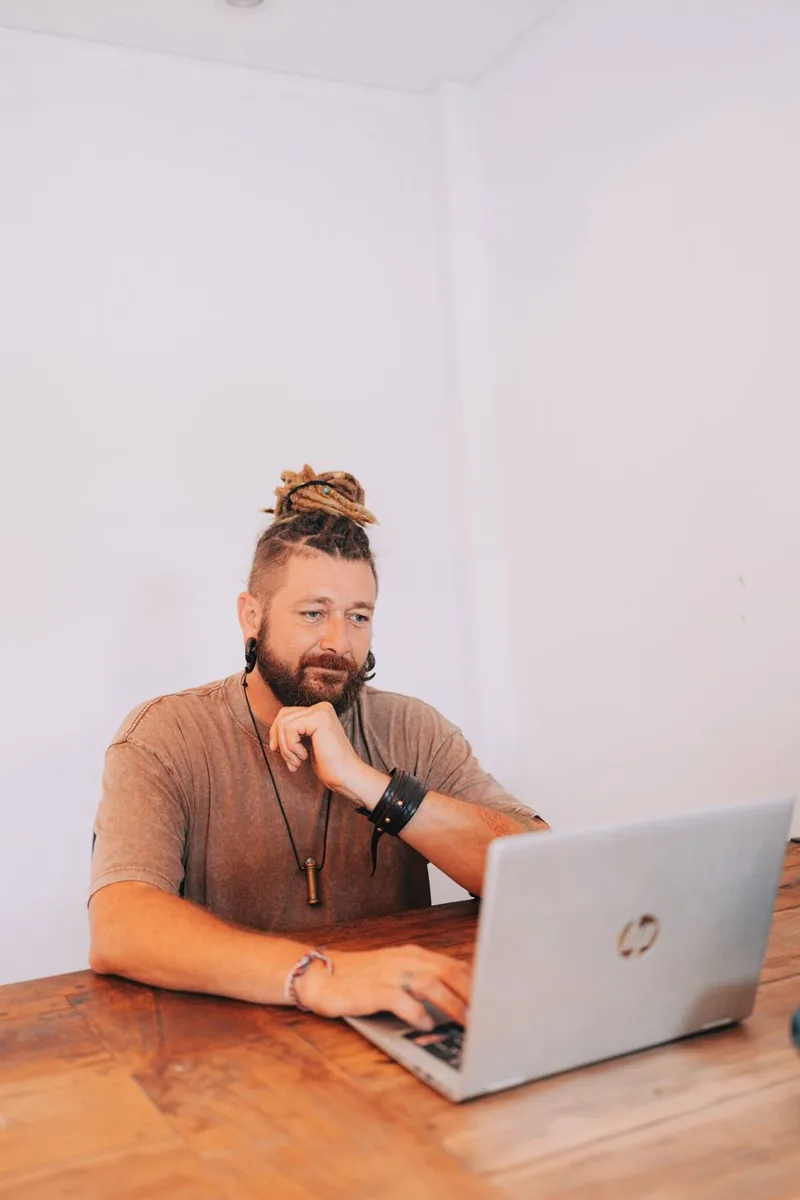 Chenzo sitting at a wooden table working on a laptop, thinking