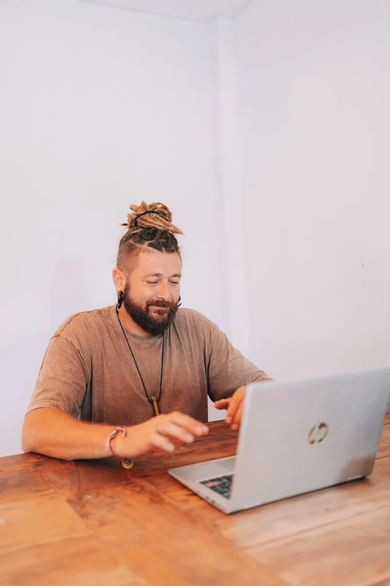 Chenzo sitzt an einem Holztisch und arbeitet an einem Laptop