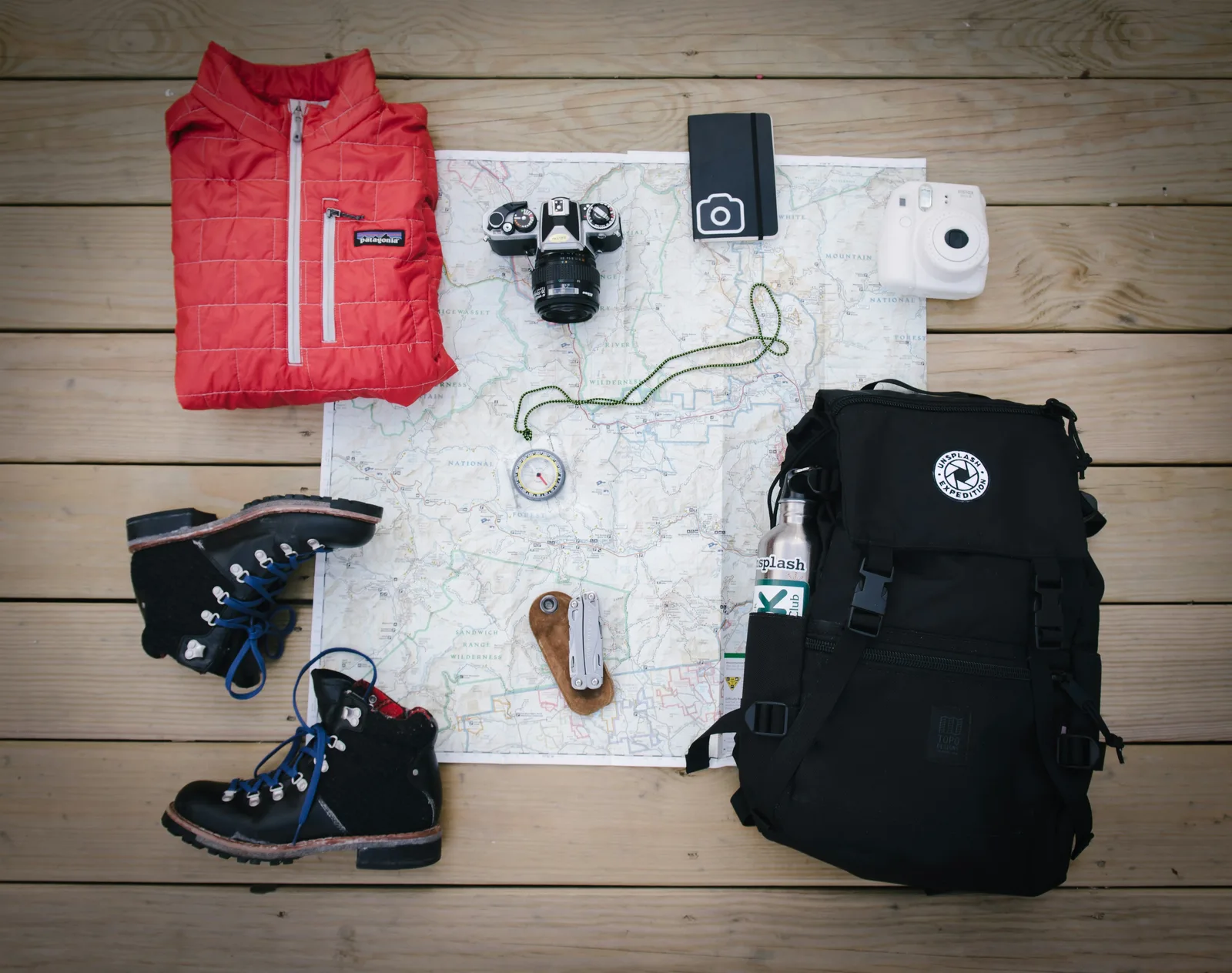 Hiking boots, backpack and map laid out on a wooden deck