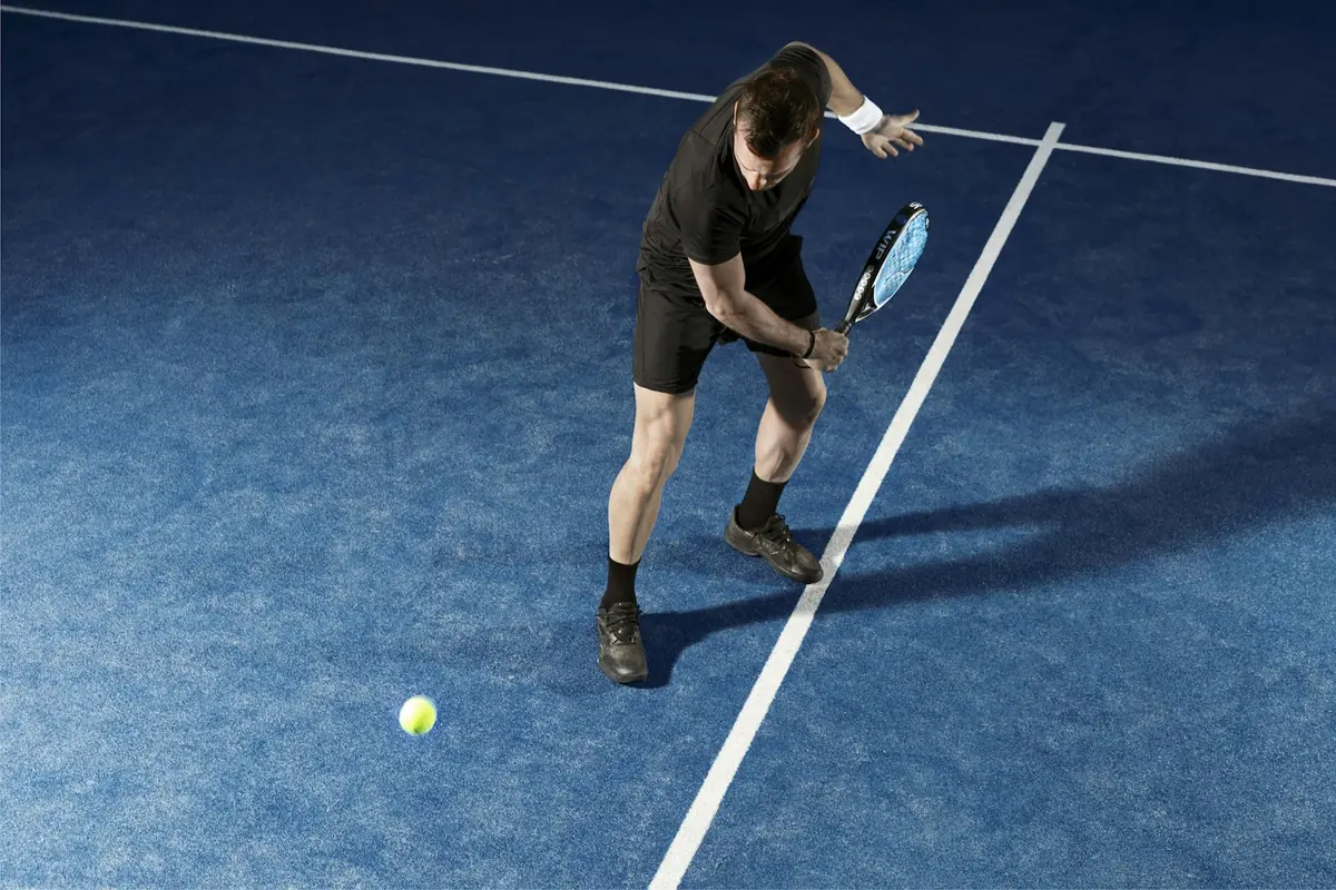Padel player preparing an underhand serve on a blue court