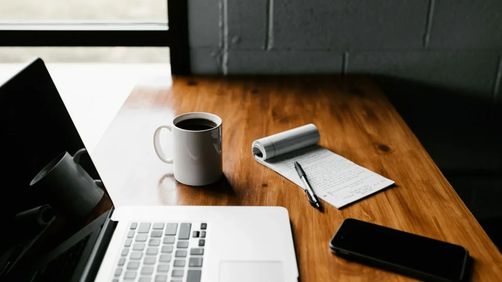 Laptop, coffee mug and phone on a wooden table, a simple remote work setup
