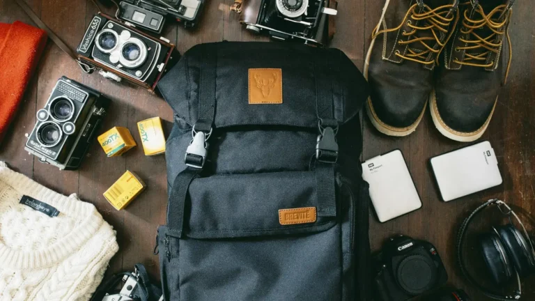 Black travel backpack laid out with cameras, hard drive and boots before packing
