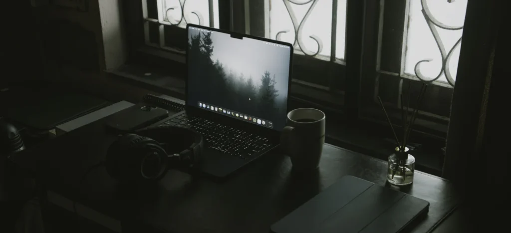 Laptop, headphones and a coffee cup on a desk by a window
