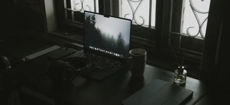 Laptop, headphones and a coffee cup on a desk by a window