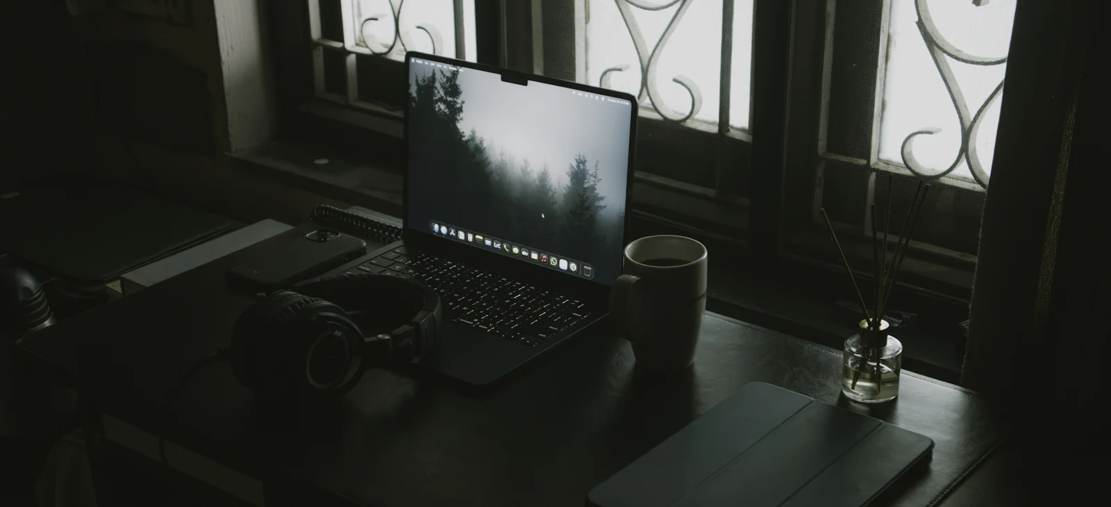 Laptop, headphones and a coffee cup on a desk by a window