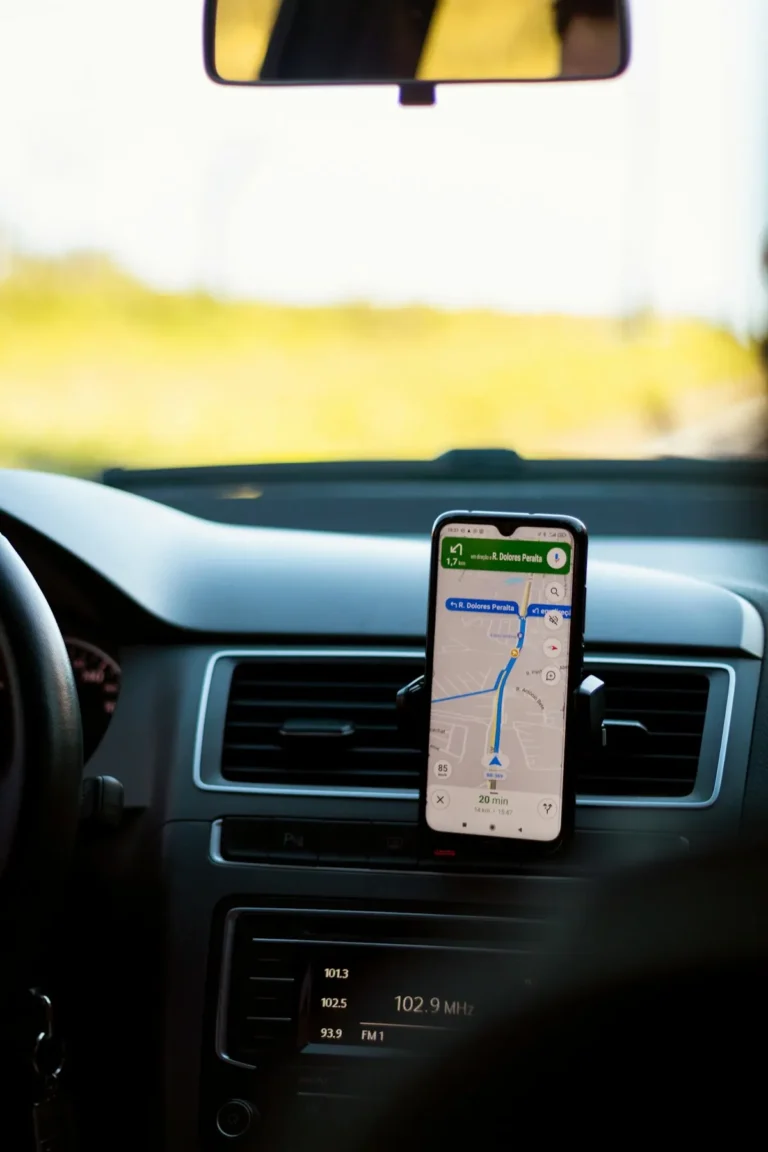 Smartphone mounted on a rental car dashboard showing turn-by-turn GPS navigation on a sunny highway