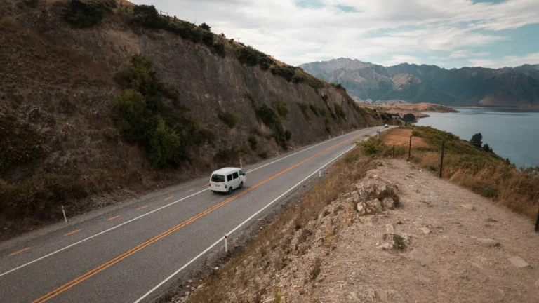 Camper van driving along a scenic lakeside road on a long road trip