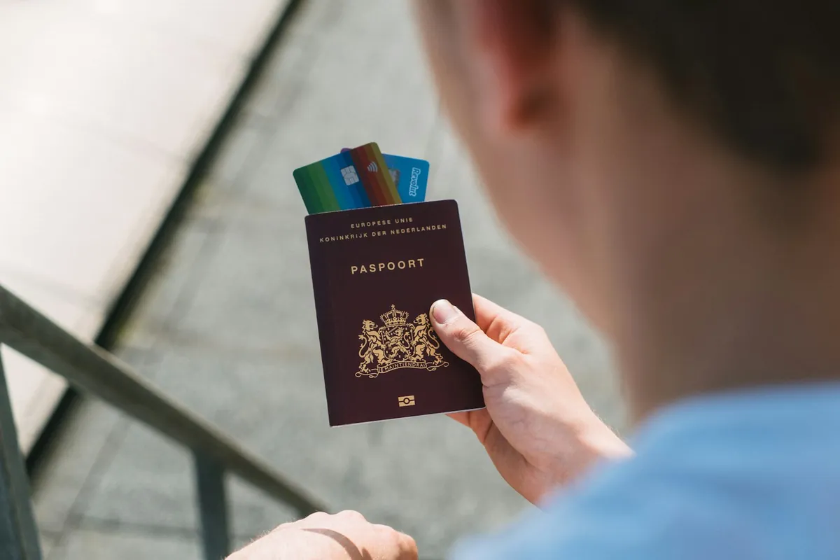 Hand holding a passport with bank cards tucked inside, seen over the shoulder