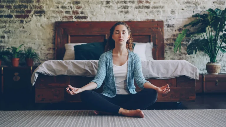 Woman meditating in lotus position on a bedroom floor