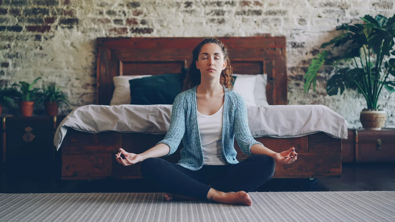 Woman meditating in lotus position on a bedroom floor