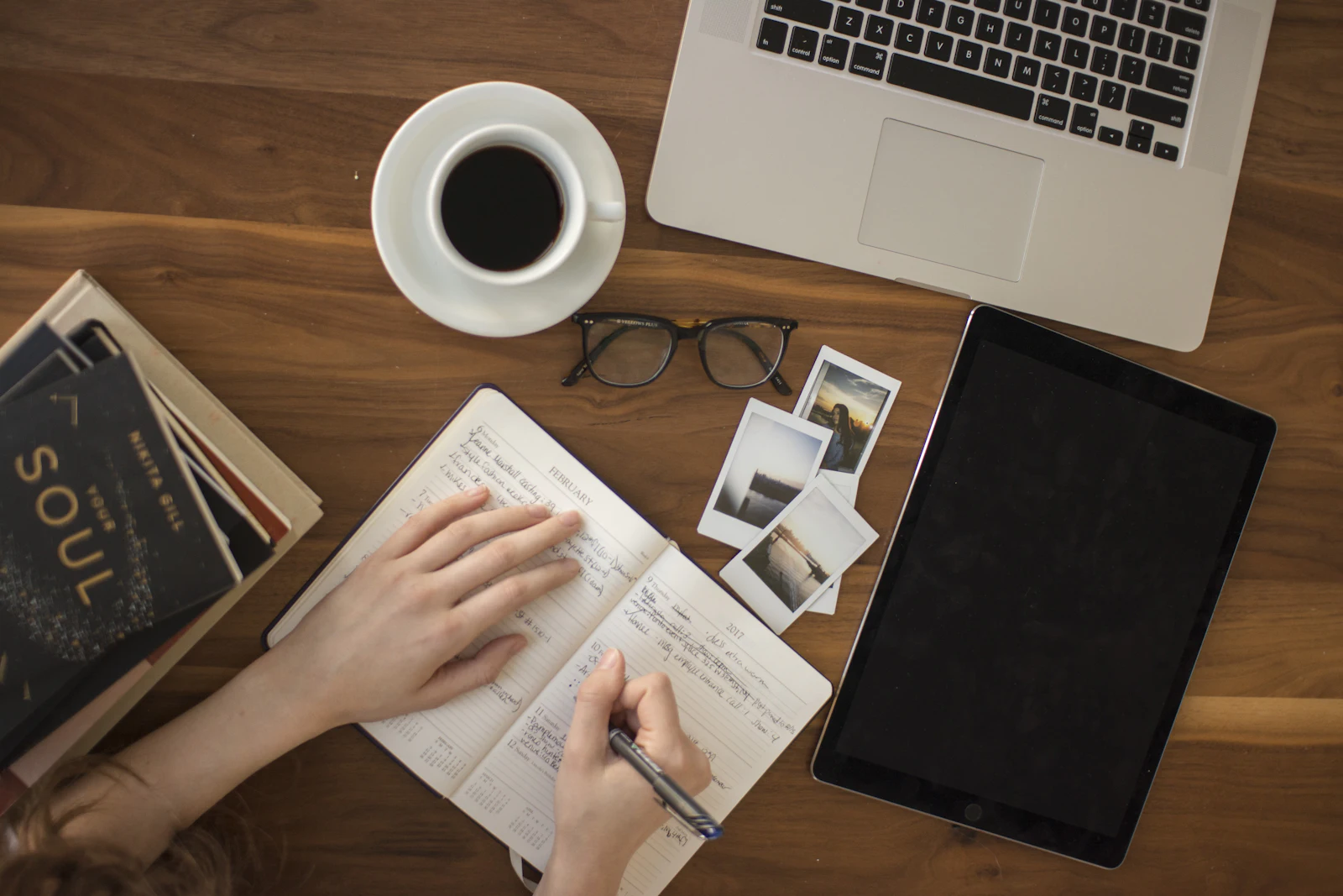 Person writing in a notebook next to a laptop and a cup of coffee