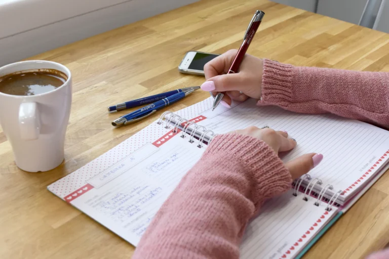 Person writing in a notebook next to a cup of coffee