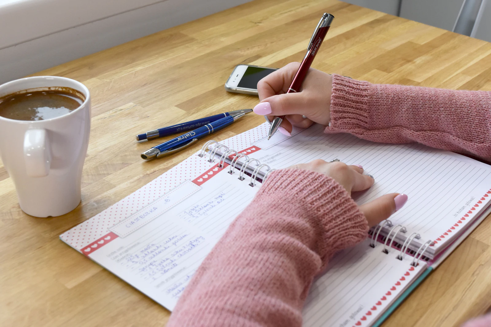 Person writing in a notebook next to a cup of coffee