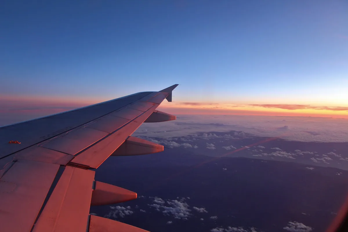 Airplane wing lit by a sunset, seen through the cabin window