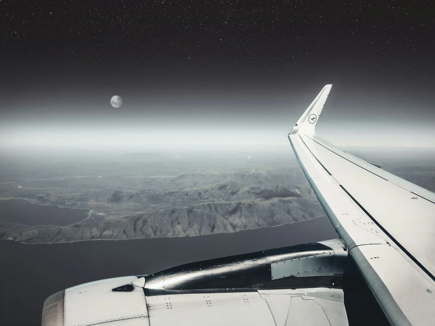 Airplane wing and engine seen from a window at night with a moon over a dark coastline