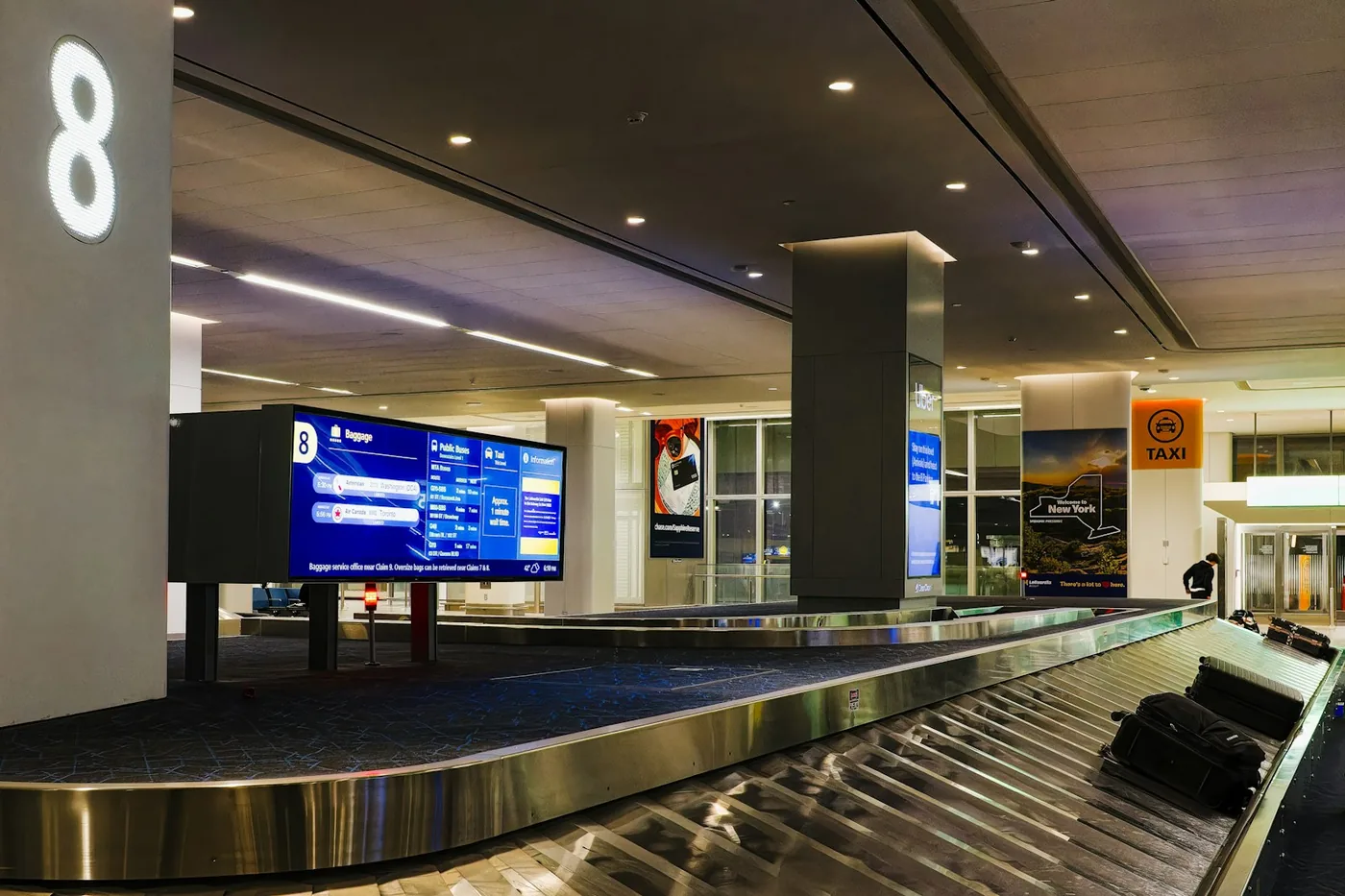 Baggage carousel in an airport arrivals hall with a flight display, the place an AirTag or SmartTag 2 earns its keep
