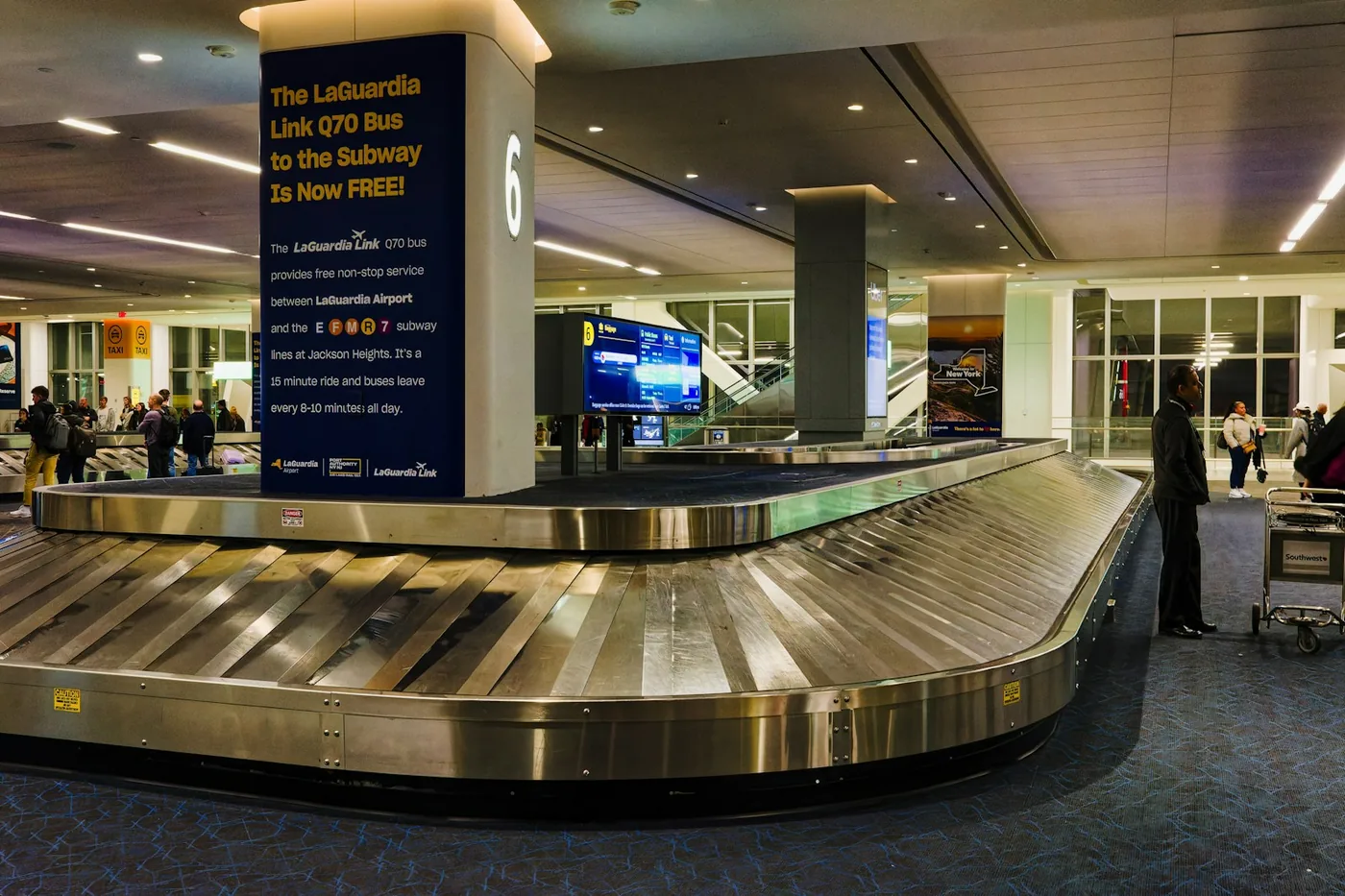 Airport baggage claim hall with a curved carousel and travelers waiting for luggage