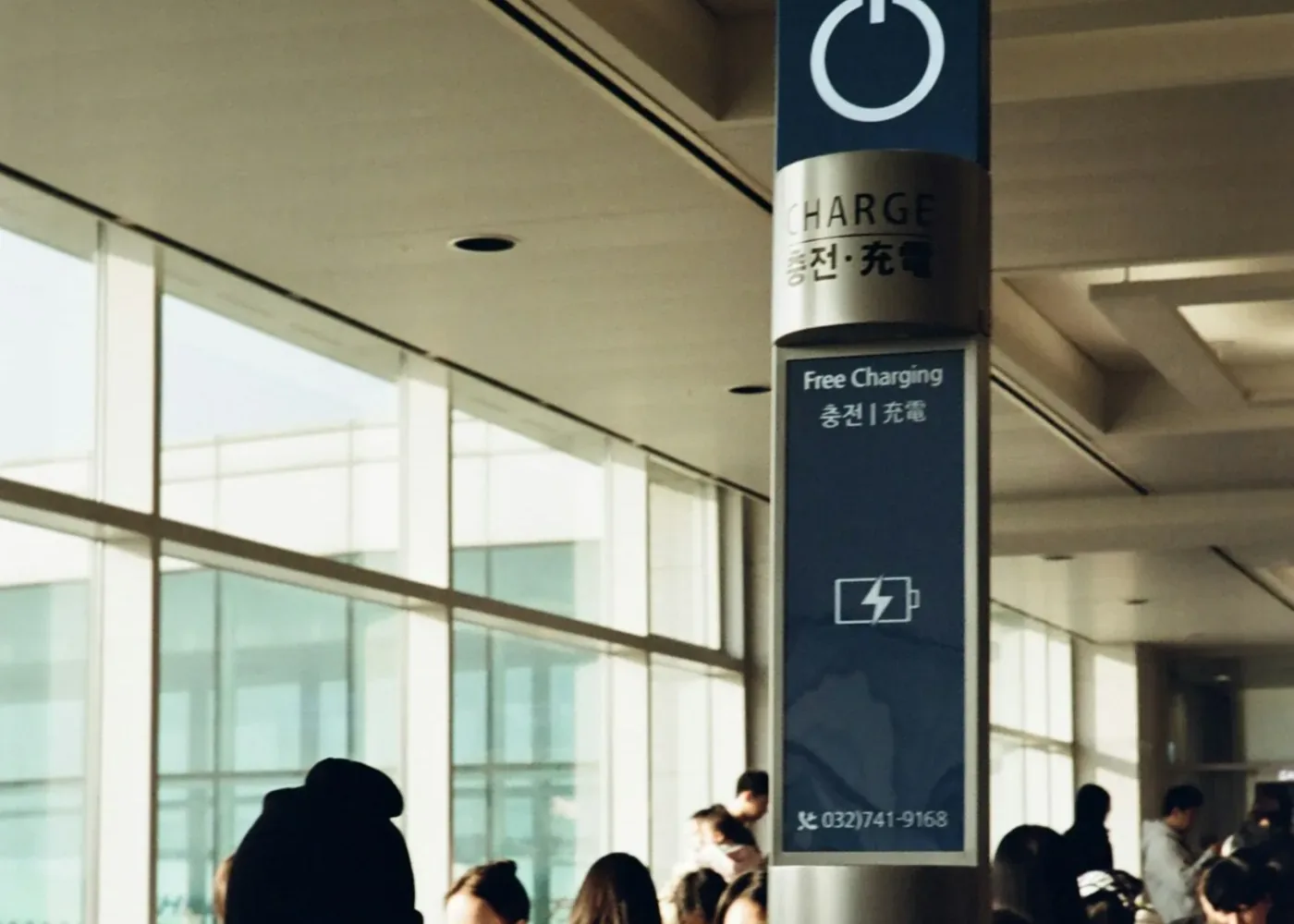 Free charging pillar in an airport hall with travelers sitting around it
