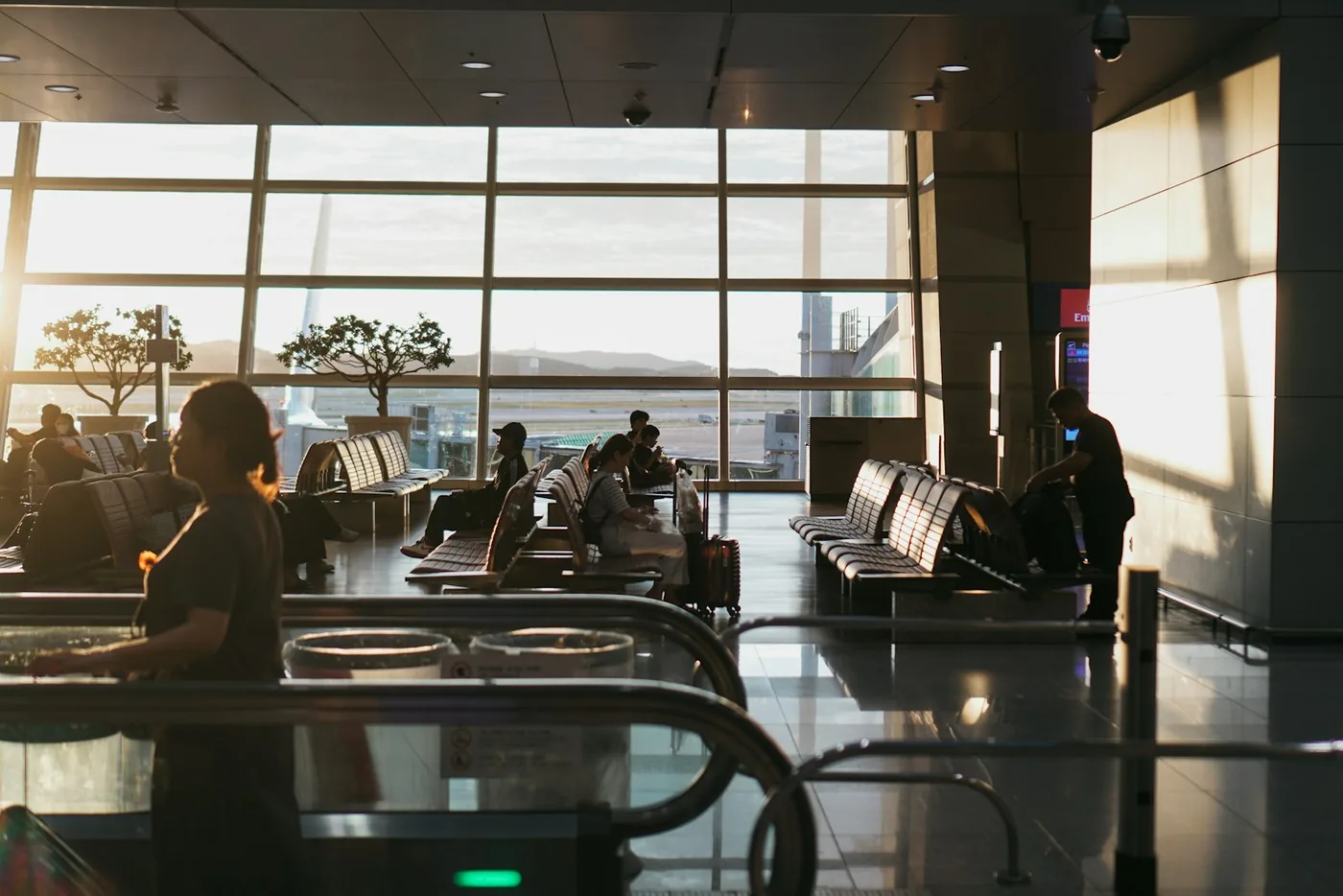 Airport hall at sunset with passengers waiting in rows of seats by large windows