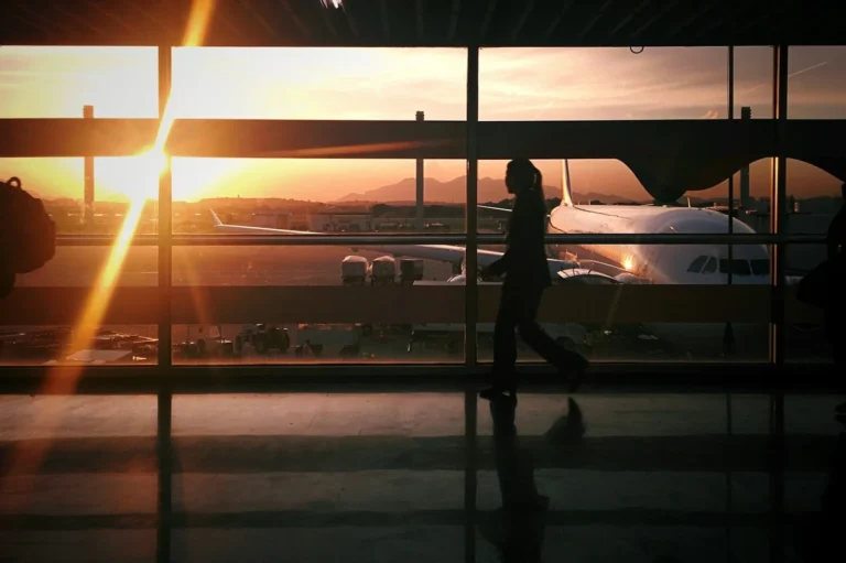 Silhouette of a traveler walking past a terminal window at sunset with an airplane outside