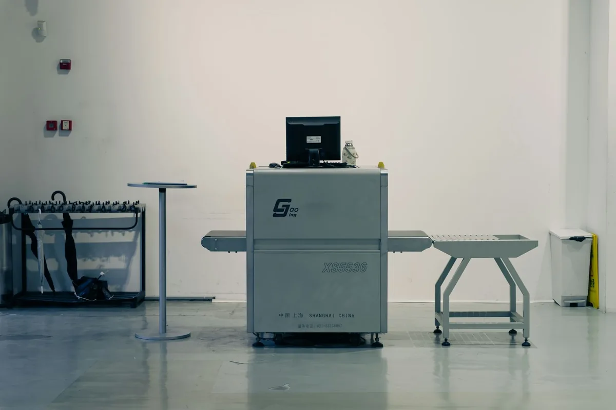 An airport style X-ray scanner with a laptop on the belt in a bright white room