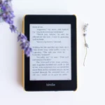 A black Kindle e-reader lying on a white surface next to a sprig of lavender