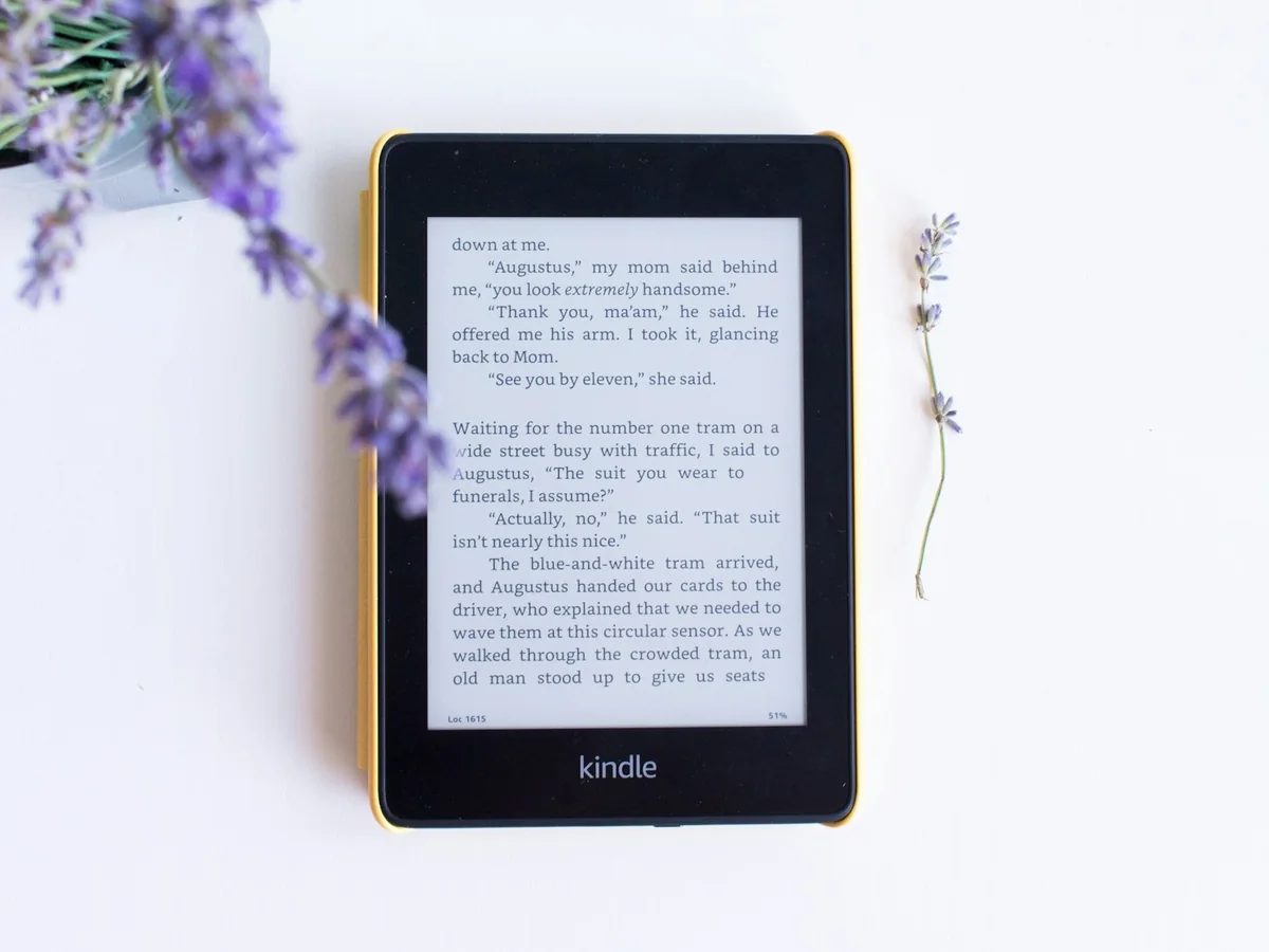 A black Kindle e-reader lying on a white surface next to a sprig of lavender