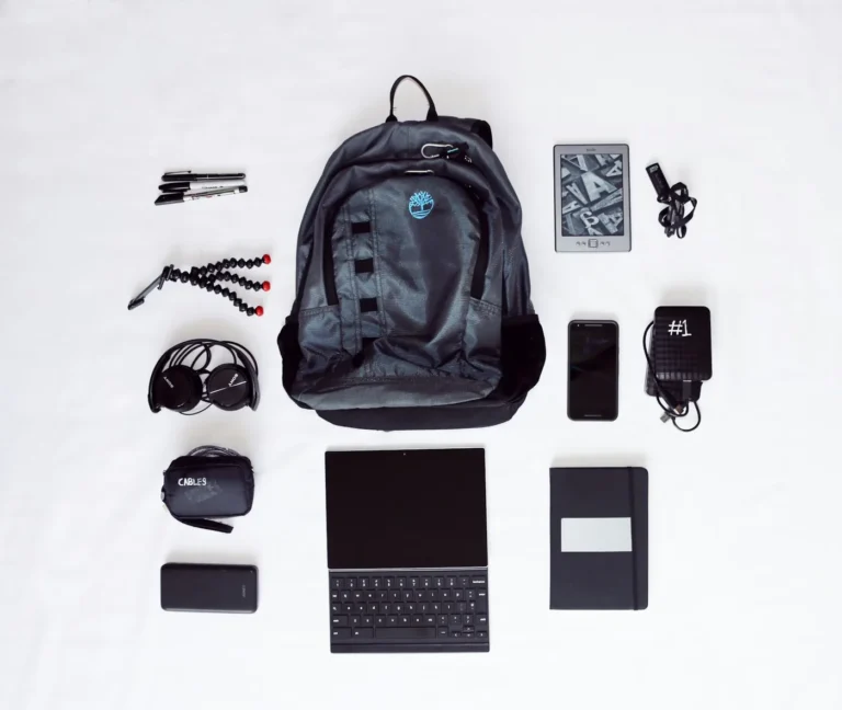 Flat lay of a backpack, headphones, smartphone, tablet with keyboard and other travel gear on a white background