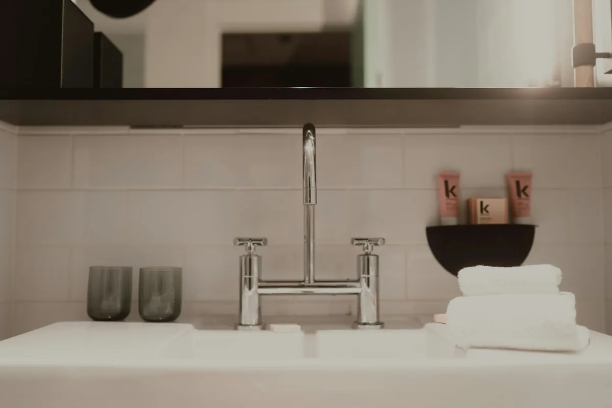 A bathroom sink with a chrome tap, two glasses and folded white towels