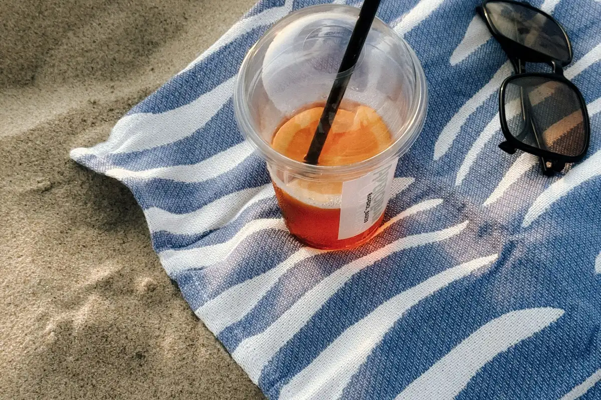 A drink with a straw and sunglasses on a striped towel on sand